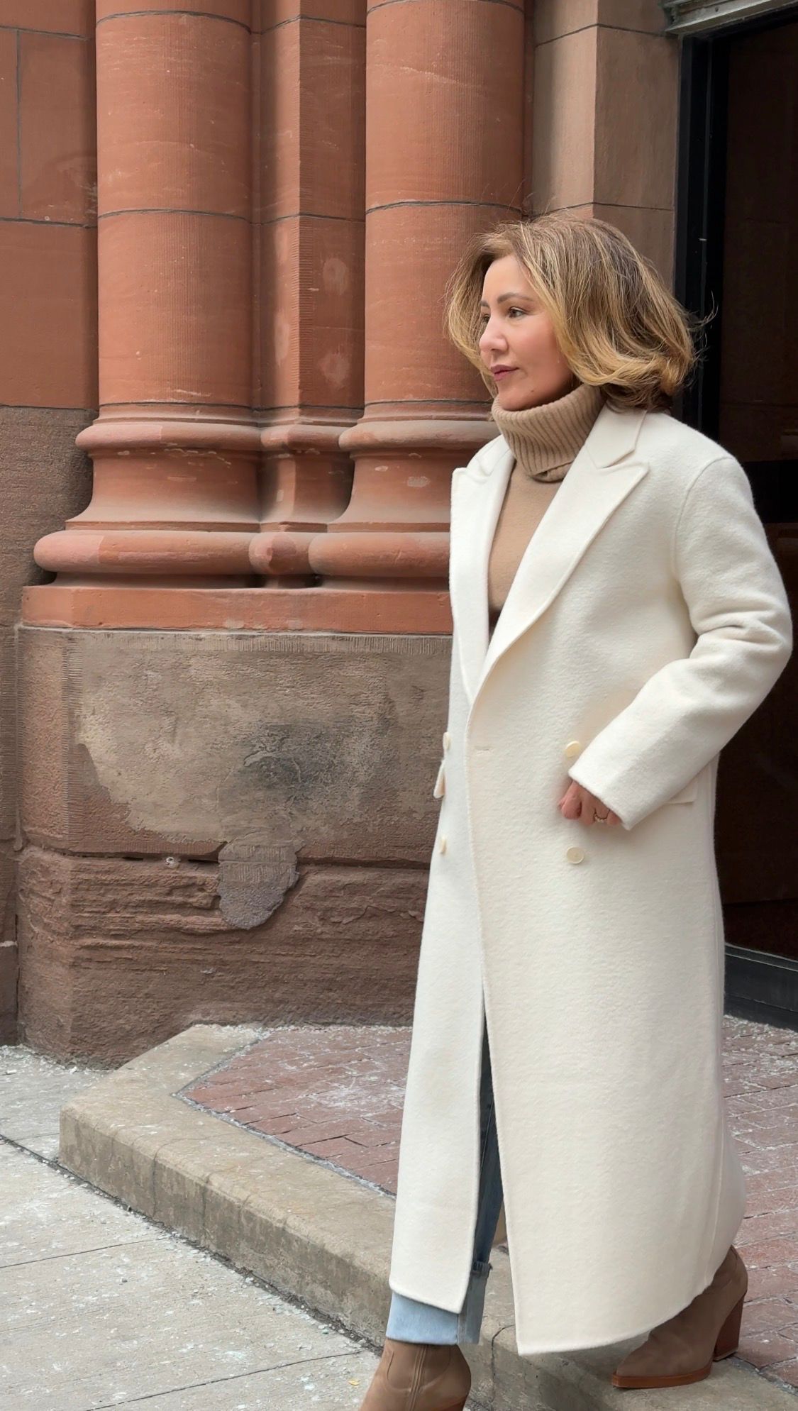 Akjemal Magtymova in a long white coat by the sandstone columns of a city building